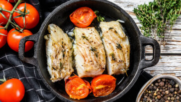 Fried cod fish fillet with spice in a cast iron pan.