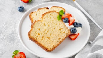 Delicious vanilla pound cake served with fresh berries and whipped cream on a gray concrete background.