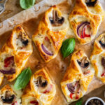Baked puff pastry with mozzarella, white mushrooms and red bell pepper on baking paper.