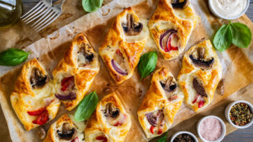 Baked puff pastry with mozzarella, white mushrooms and red bell pepper on baking paper.