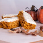 Pumpkin bars topped with cream cheese frosting surrounded with leaves, acorns, pumpkins and fall decor.