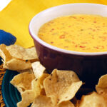 Bowl of warm queso (cheese dip) with a plate of tortilla chips