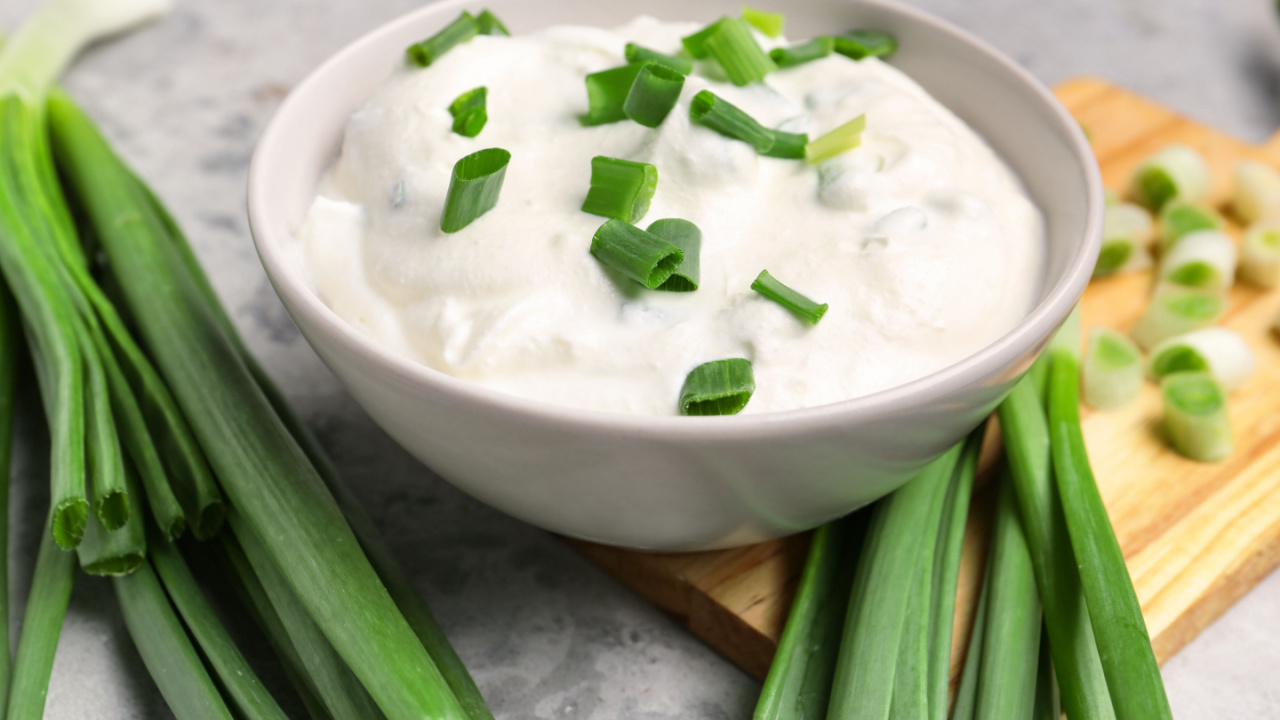 Bowl of tasty sour cream with green onion on table