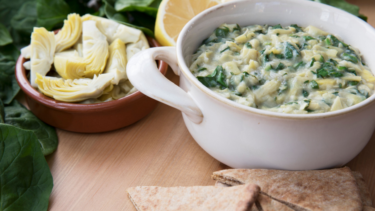 Bowl of vegan spinach artichoke dip with pita and ingredients.