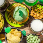 Irish St Patrick`s day beer, ale glasses, snacks, appetizer, green burger, wooden bar table with shamrock, clover, coins, leprechaun hat.