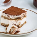 Tiramisu cake dessert served with coffee, biscuit and cocoa as ingredients on a bright white background.