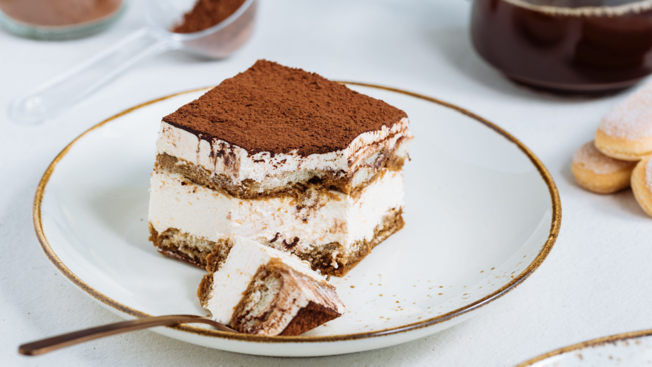 Tiramisu cake dessert served with coffee, biscuit and cocoa as ingredients on a bright white background.