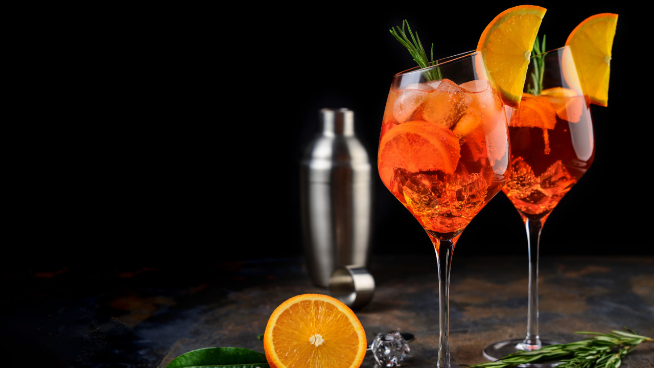 Wineglass of ice cold Aperol spritz cocktail served in a wine glass, decorated with slices of orange and rosemary branch.