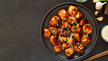 Teriyaki chicken on plate over black stone background with free text space.