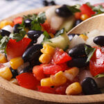 Mexican vegetable salad with black beans, corn and tomatoes macro in a wooden plate.