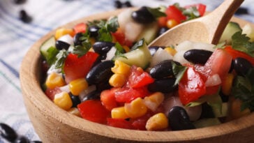 Mexican vegetable salad with black beans, corn and tomatoes macro in a wooden plate.