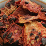 Slices of red dehydrated watermelon pulp pieces at white bowl on green background.