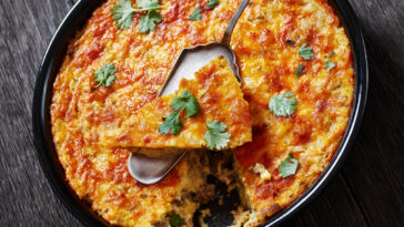 Grits casserole with ground beef meat in baking dish on dark wood table