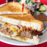 Meatloaf sandwich with melted cheddar cheese and a side salad.