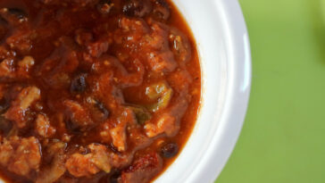tasty turkey pumpkin chili in white bowl with green background