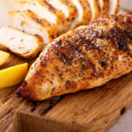 Grilled chicken breast with spice rub and lemon on a cutting board, sliced and whole