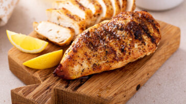 Grilled chicken breast with spice rub and lemon on a cutting board, sliced and whole