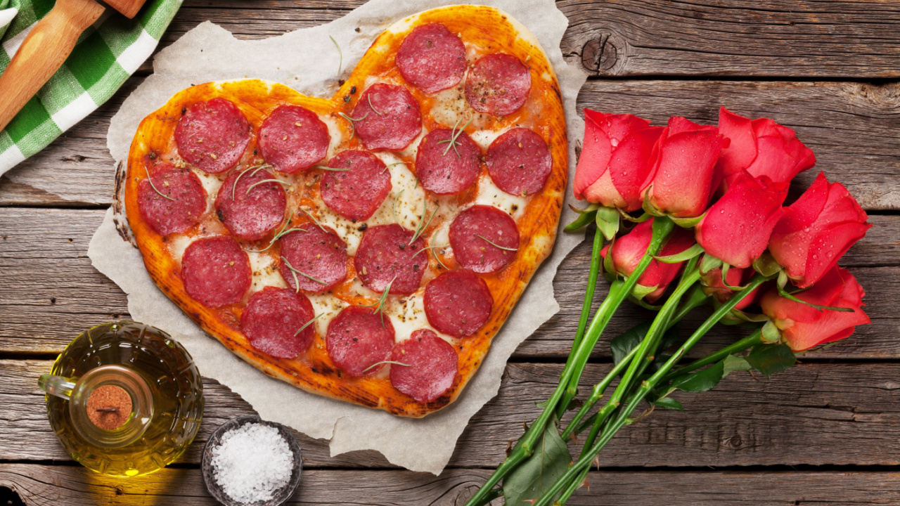 Heart shaped pizza with pepperoni and mozzarella and red rose flowers bouquet.